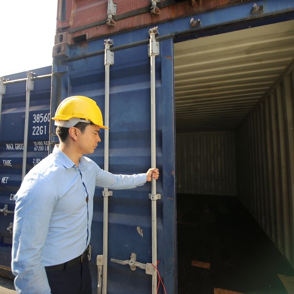 Workers carefully loading wooden furniture into a shared shipping container for LCL (Less than Container Load) transport, securing items with protective padding and straps.