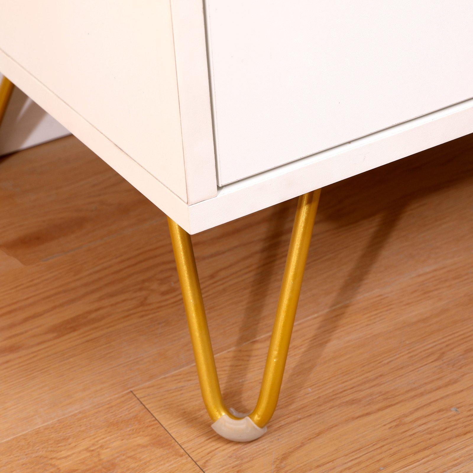 Modern white bedside table with sleek drawer and wooden legs next to a cozy bed
